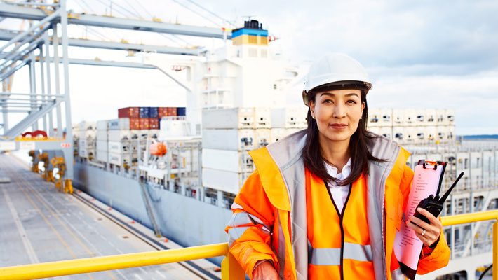 A supply chain professional smiles as she oversees a shipment of compliant parts in a shipping yard.