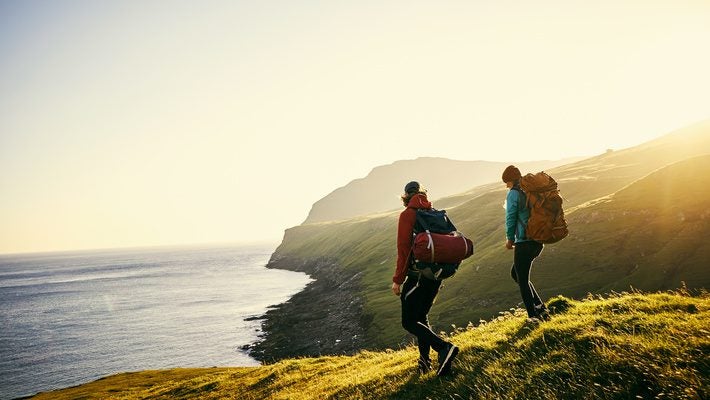 Two hikers explore a coastal cliffside, symbolizing the connection between sustainable practices and environmental preservation, a key focus of EU ESG regulations.